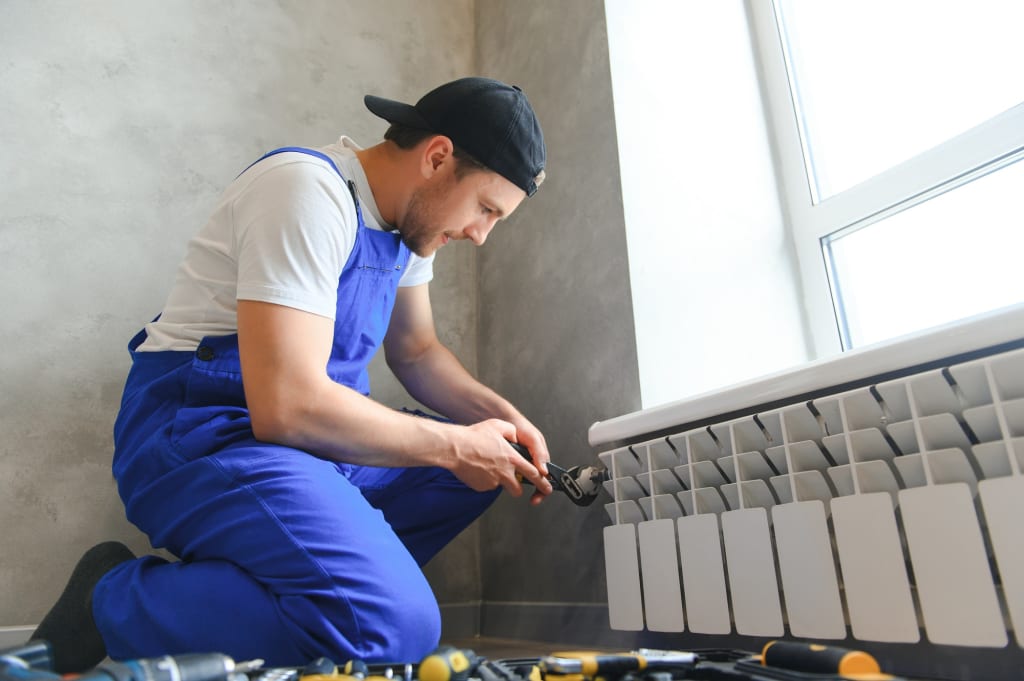 young man plumber checking radiator while installing heating system in apartment
