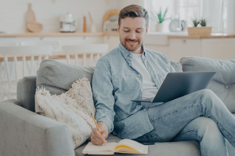 Young office worker working remotely from home researching using notebook and taking notes