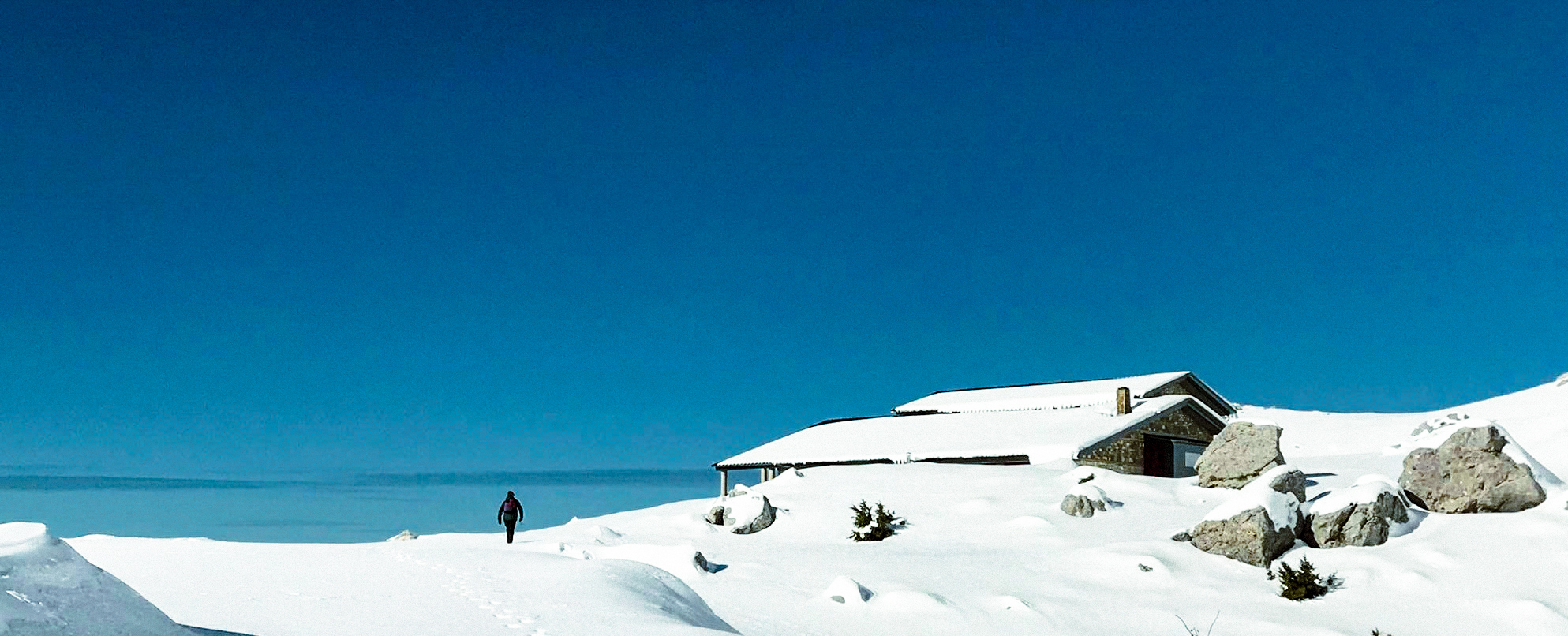 Refuge from afar with a man walking towards it. Winter. Meters of snow.