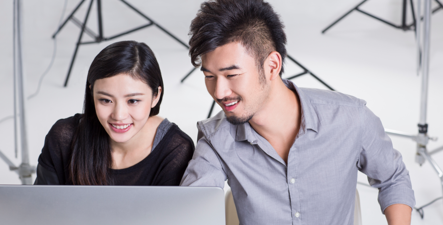 Two smiling young professionals reviewing vital records online on a laptop in a studio setting, exploring secure, legitimate online notarization services for official documents.