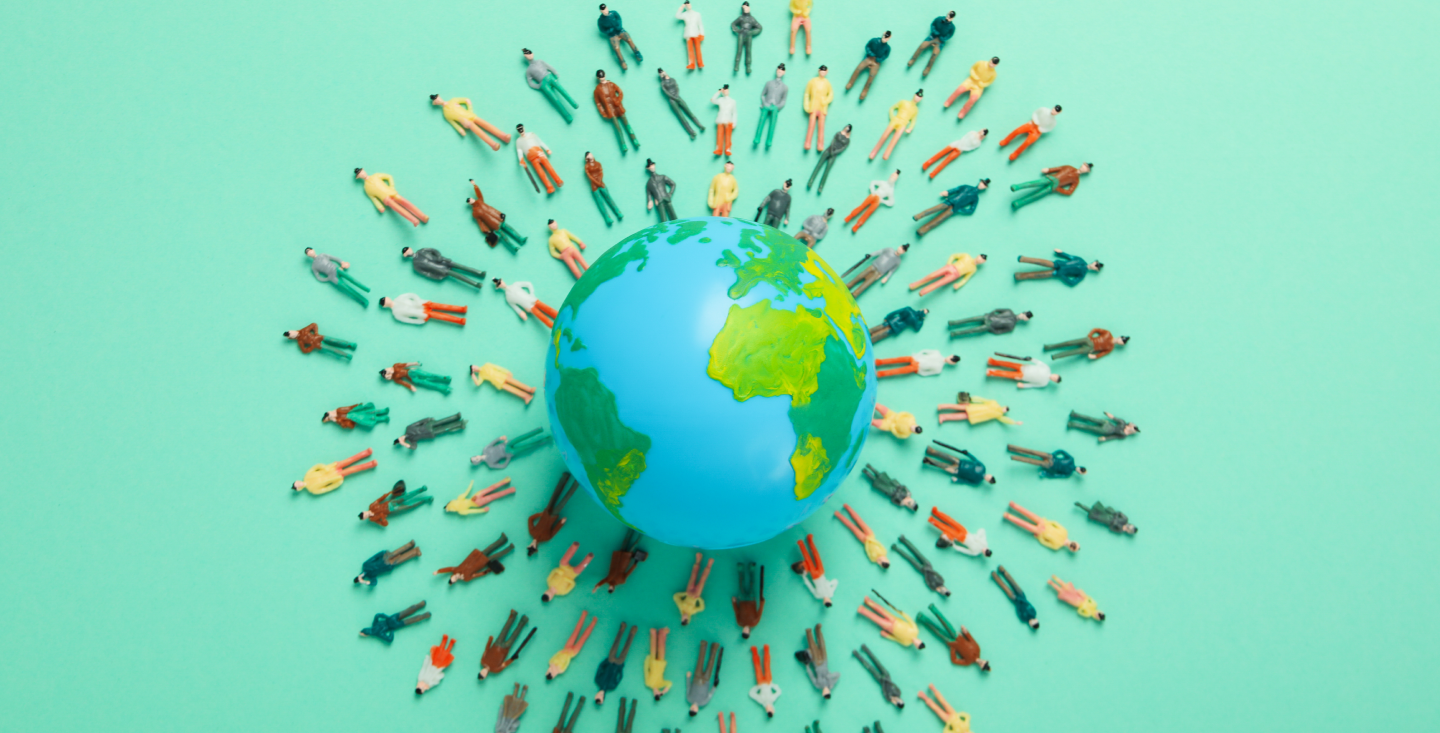 global citizenship Miniature figurines of diverse people arranged in a circular pattern around a globe on a mint green background, symbolizing global population and unity.