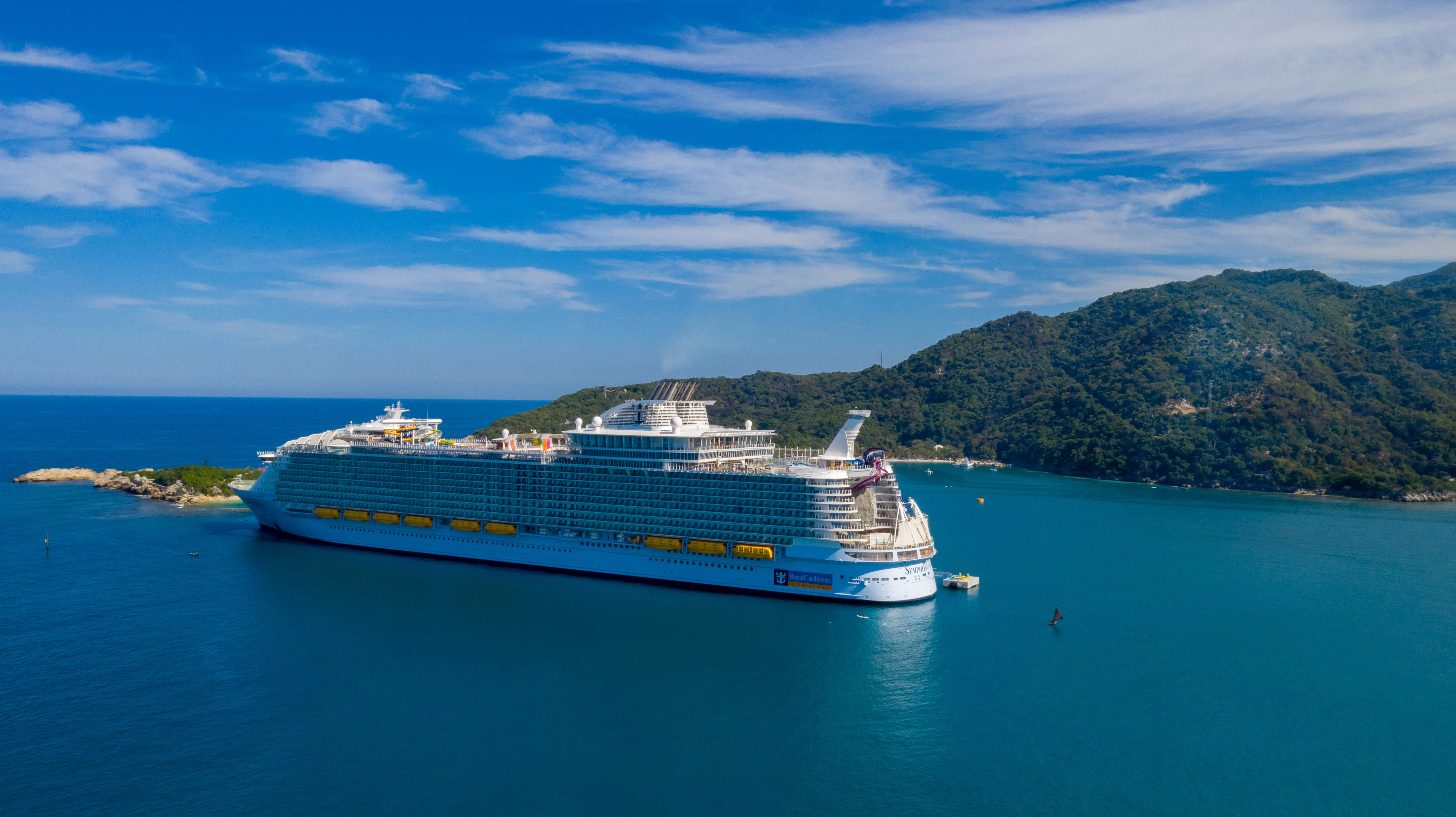 Large Royal Caribbean cruise ship sails across crystal blue waters during a beautiful day