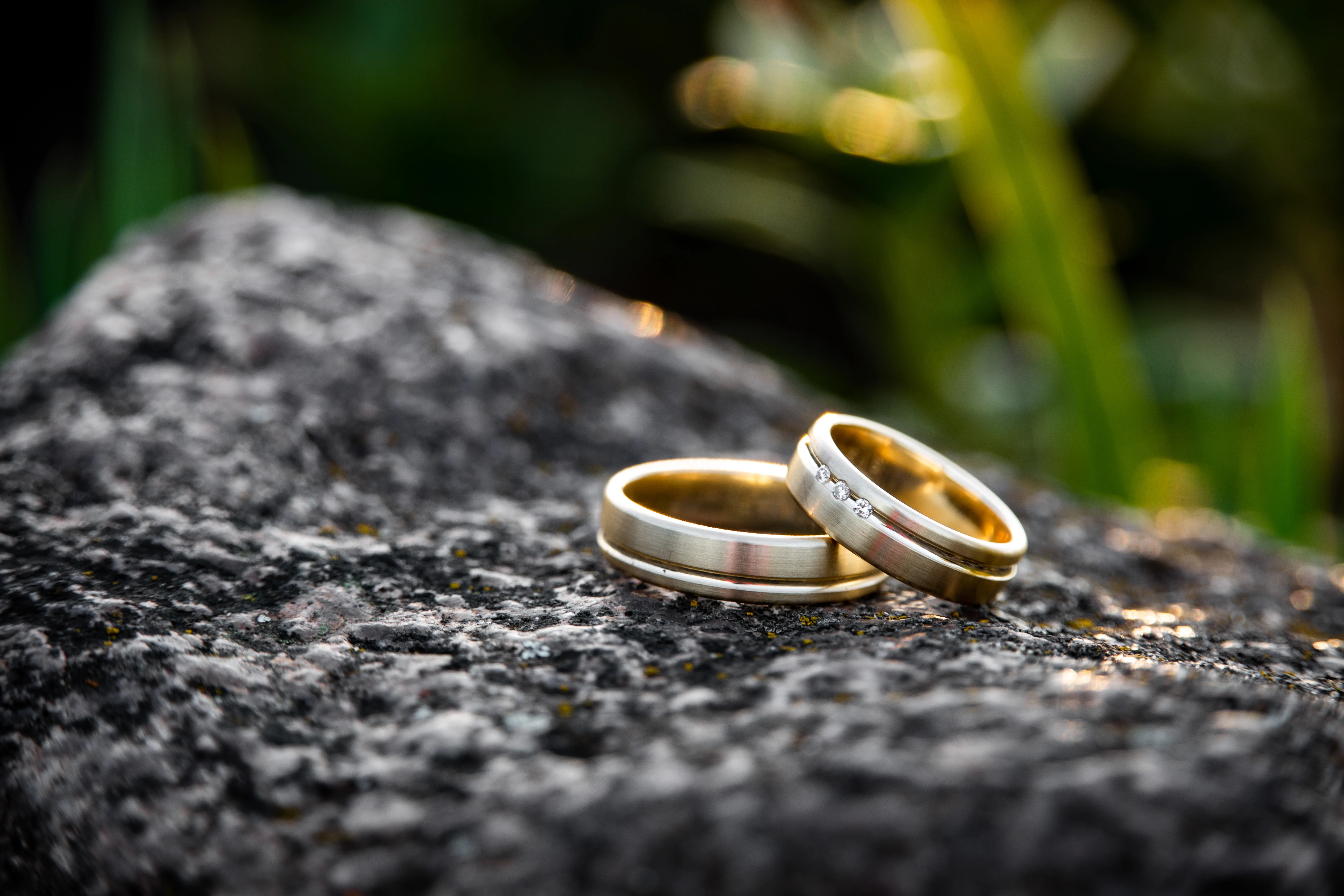 two wedding rings placed together ontop a a rock in nature.