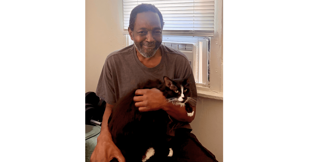 ** Man holding gray and white cat indoors next to new air conditioning unit