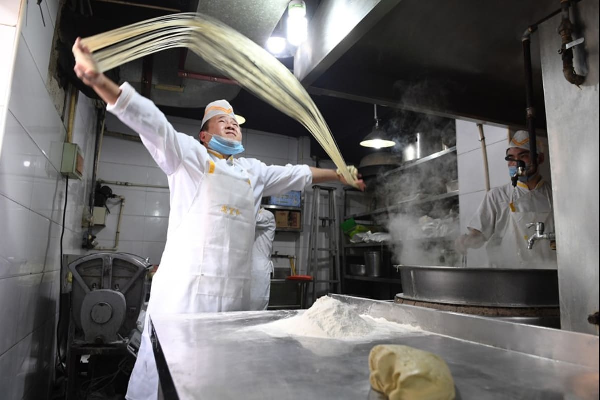 Chef hand-pulling traditional Lanzhou beef noodles into thin strands at busy restaurant
