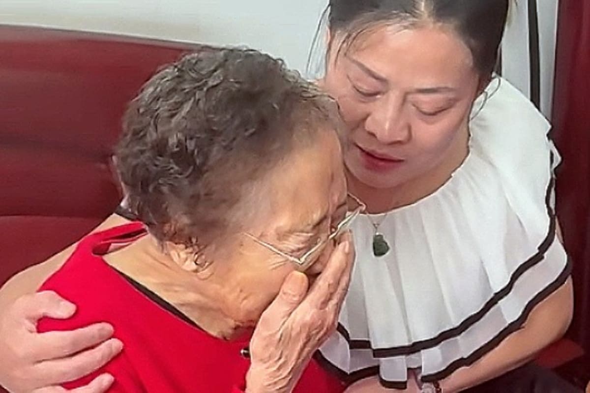 Elderly Chinese woman in golden traditional coat holds hands with younger woman during emotional family reunion