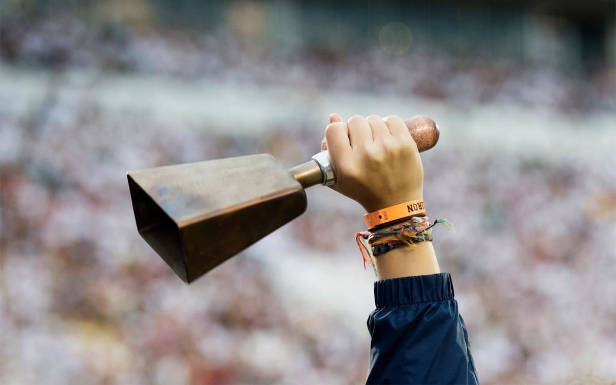 Mississippi State football fans holding cowbells in stadium wearing white during game