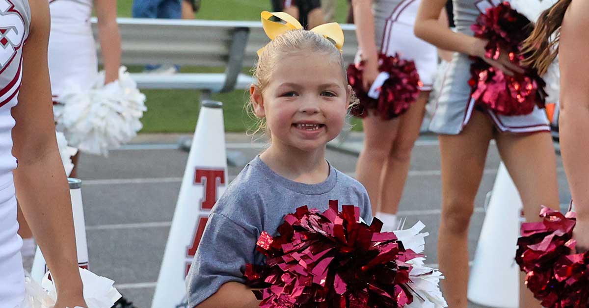 Five-year-old cancer survivor Kinslee Gibson cheering with Tate High School cheerleaders wearing yellow ribbons