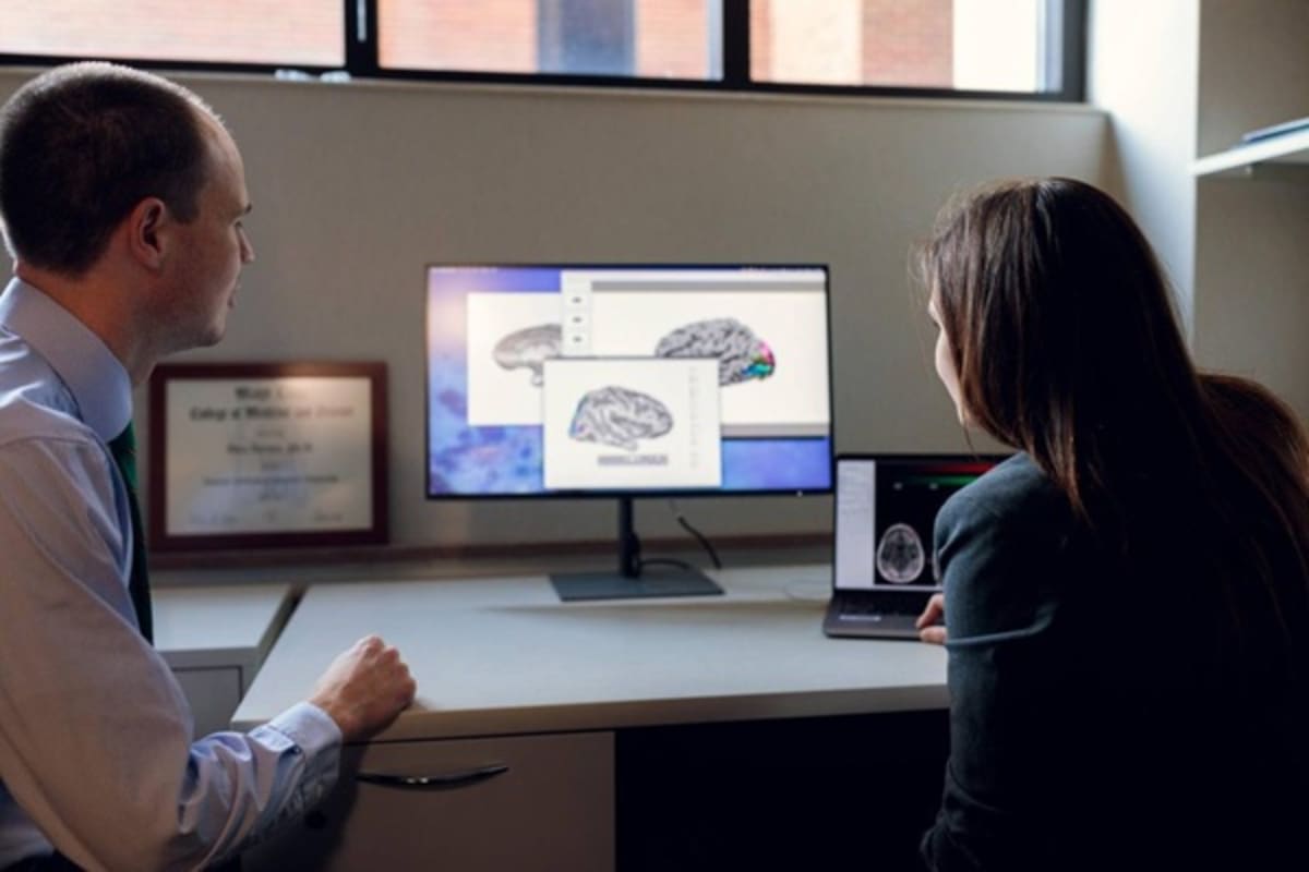 Two researchers examining detailed brain imaging scans on computer screen in medical laboratory