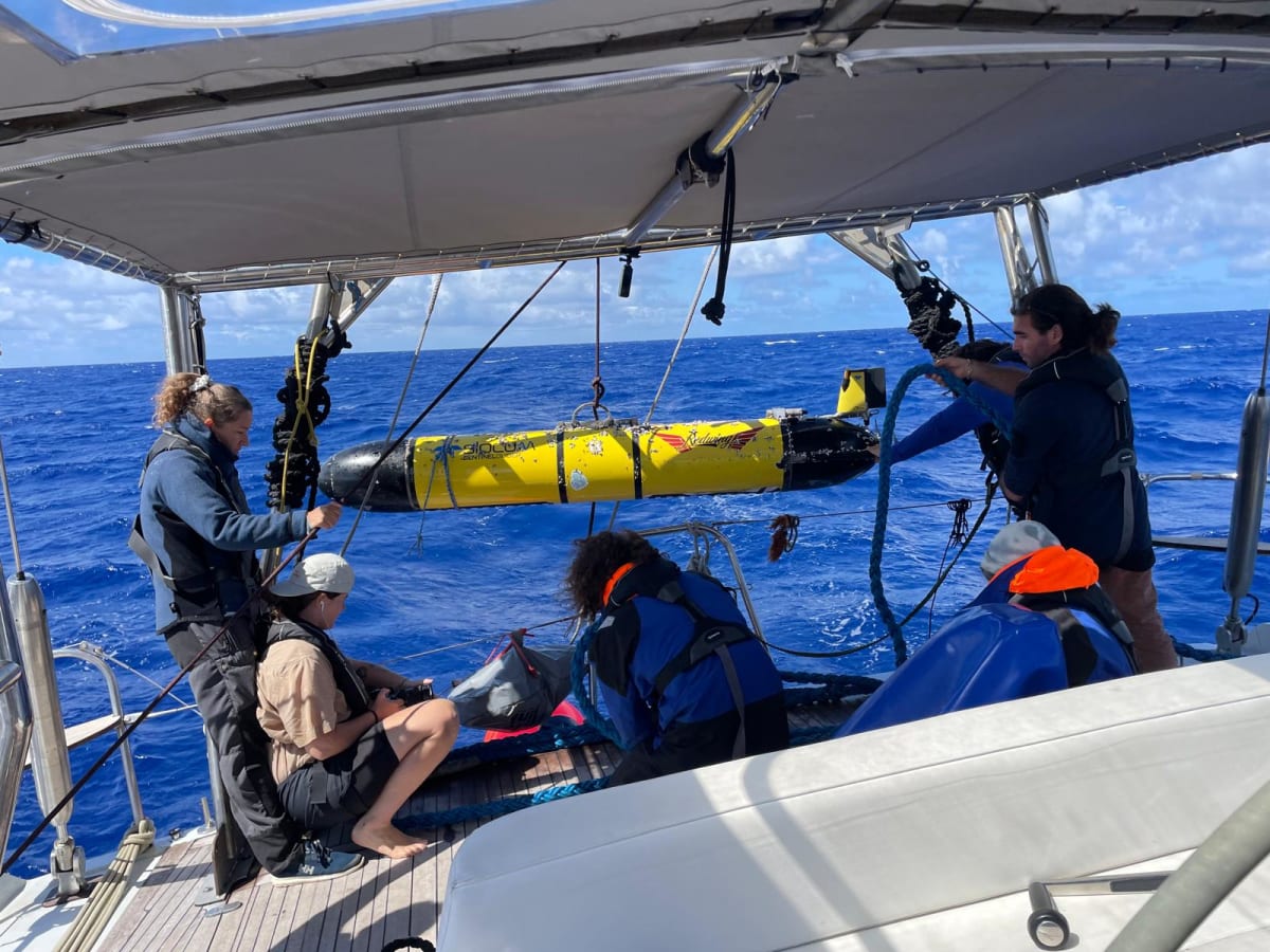 Crew members on sailing vessel pulling small yellow underwater research glider from ocean