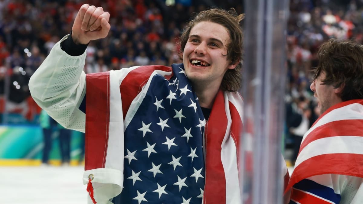 Jack Hughes wrapped in American flag celebrating Olympic gold medal with bloodied smile