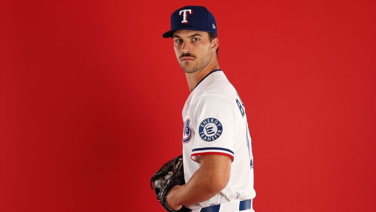 Texas Rangers pitcher Carter Baumler smiling on mound surrounded by teammates celebrating roster news