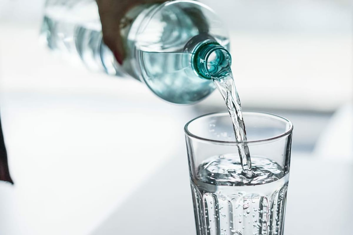 Clear glass of fresh drinking water with water-from-air device in background