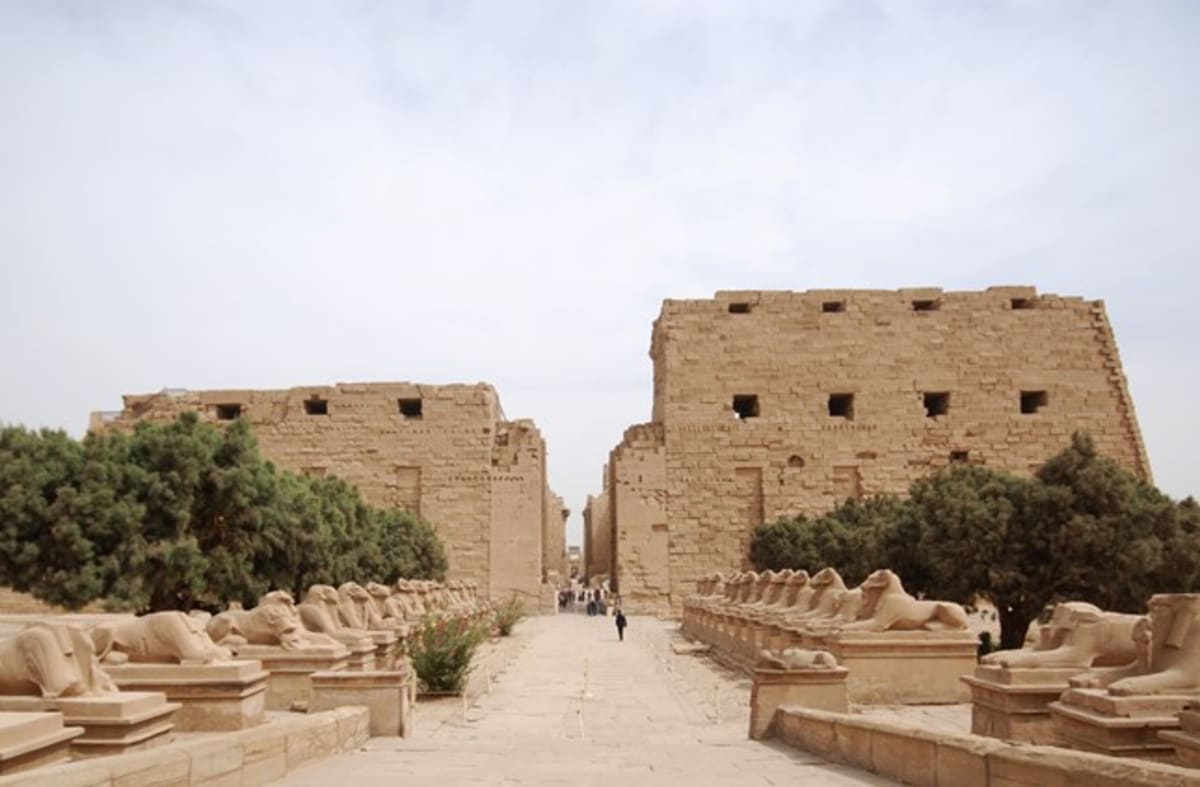Sunset rays streaming through ancient stone columns at Karnak Temple during summer solstice alignment
