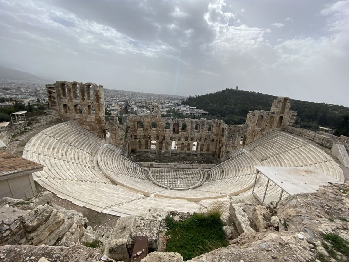 Ancient stone amphitheater with curved seating tiers beneath the Acropolis at sunset in Athens