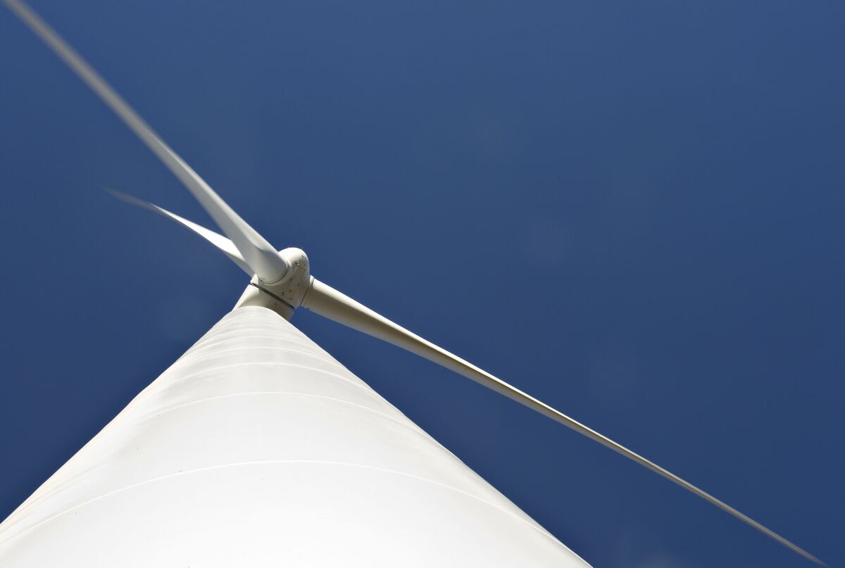 Tall white wind turbines spinning against blue sky in rural India countryside