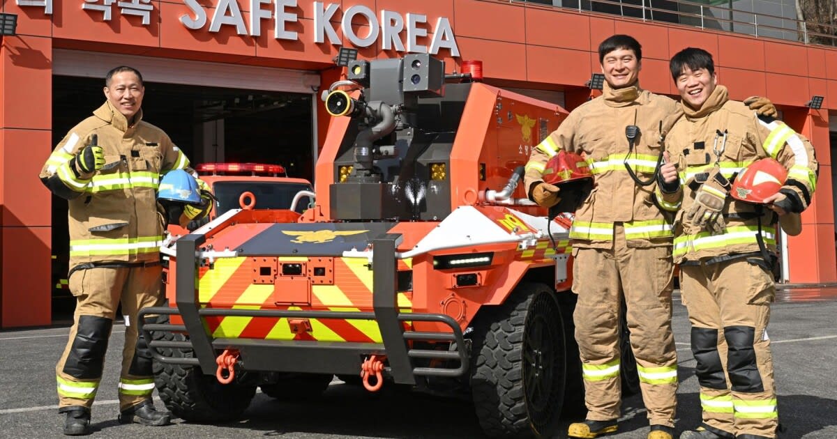 Six-wheeled autonomous firefighting robot surrounded by firefighters in uniform at South Korean station