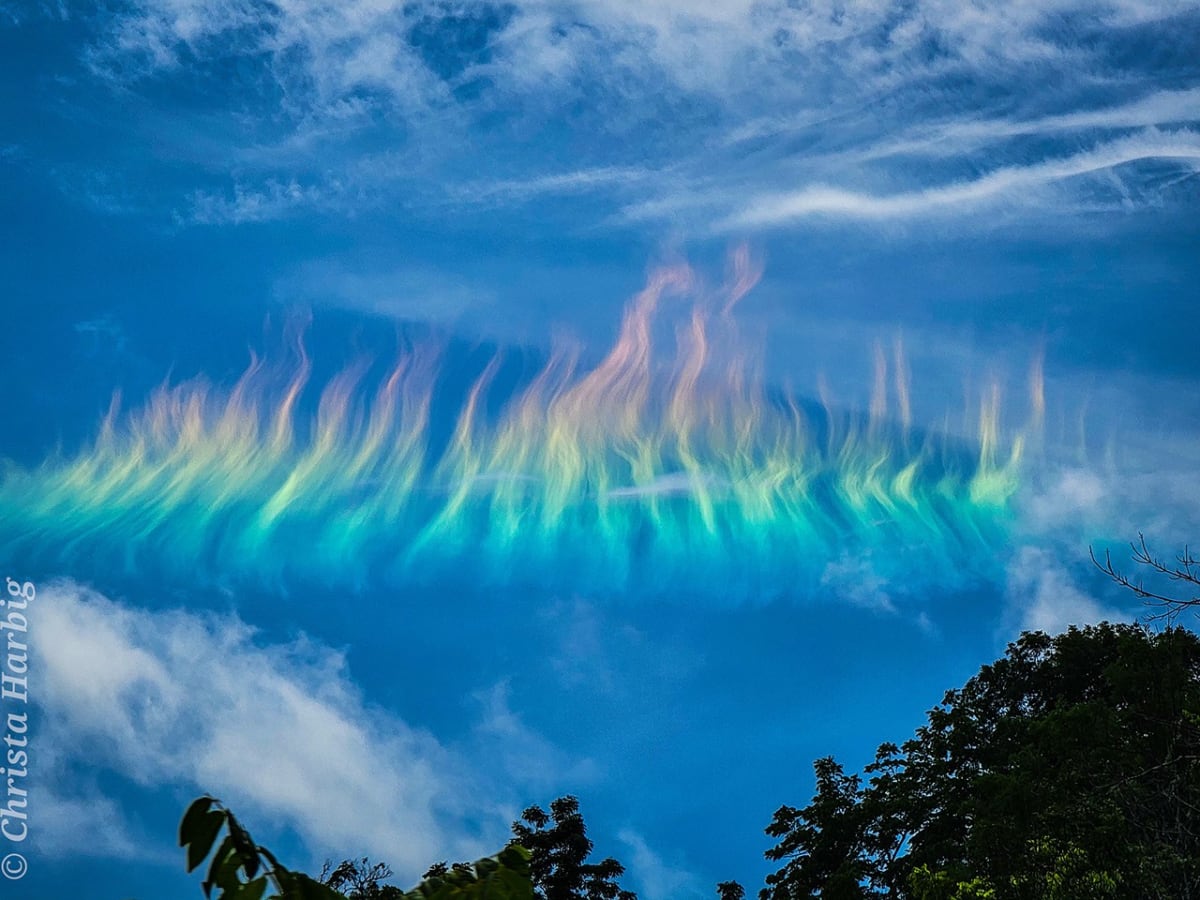 Colorful fire rainbow arc stretches horizontally across blue sky above West Virginia mountain