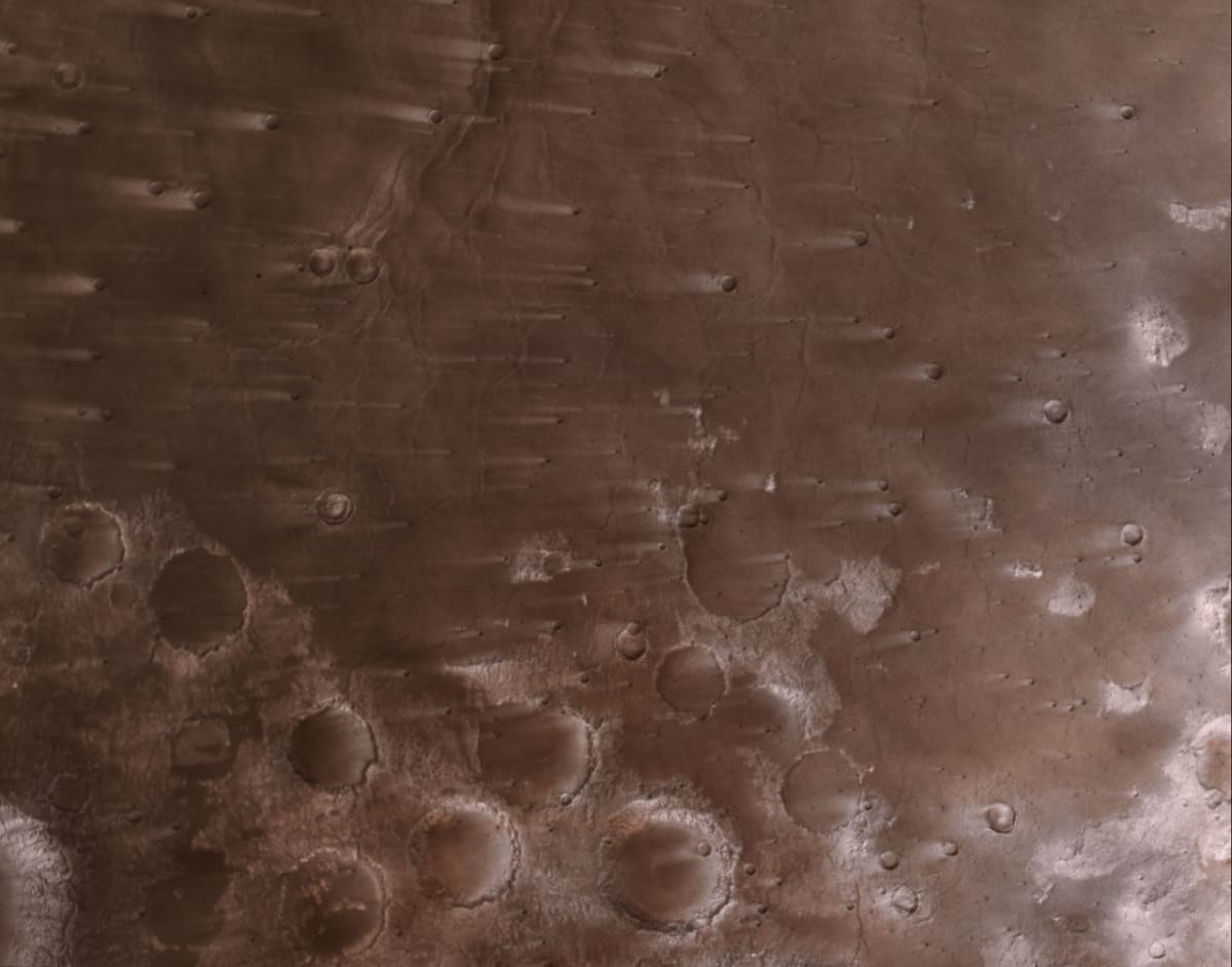 Mars surface showing long wind-blown streaks across ancient impact craters captured by NASA Psyche spacecraft