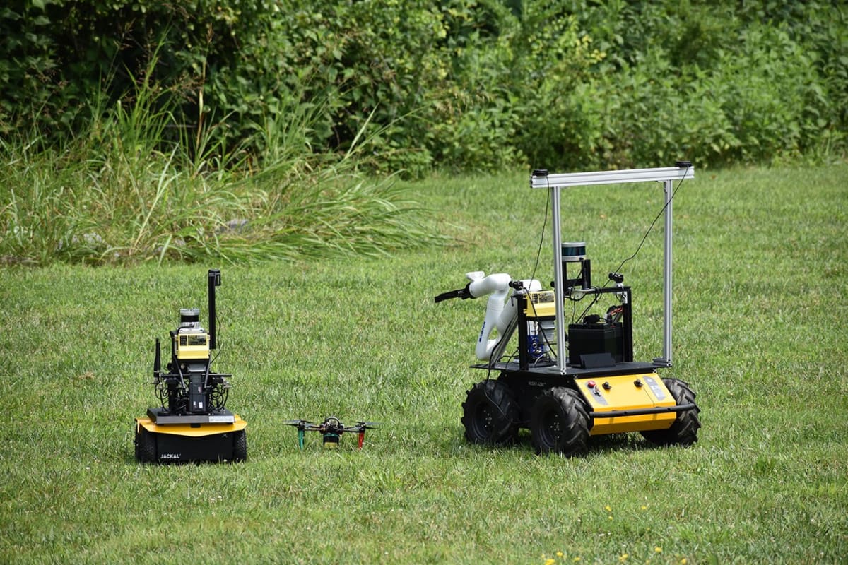 Five NASA scientists stand with drone and two rovers during ASTRA field test in Virginia