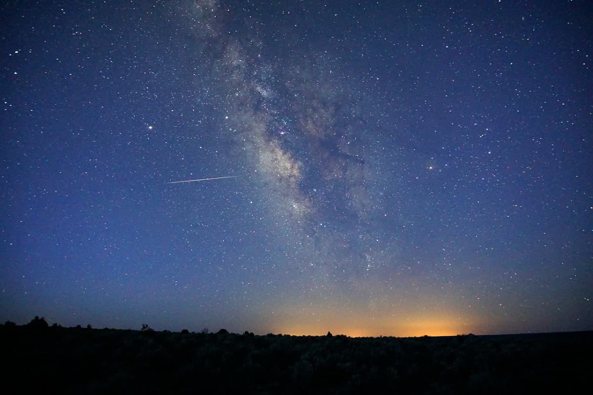 Night sky showing meteor shower streaks and bright comet tail over dark horizon