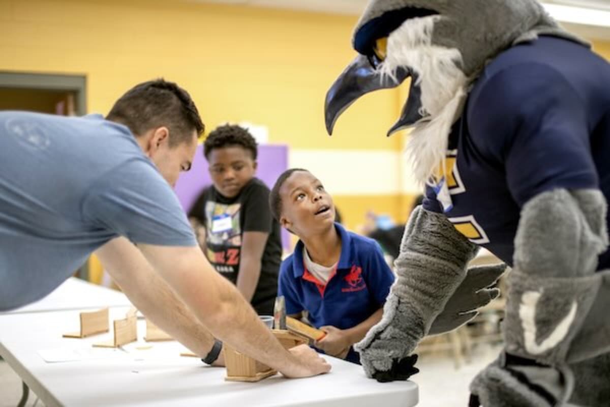 College students and children building colorful wooden birdhouses together at community center table