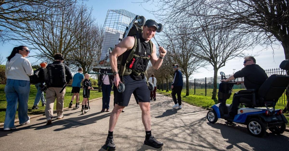 Pastor James Baker walking on outdoor track wearing shopping cart loaded with groceries on his back