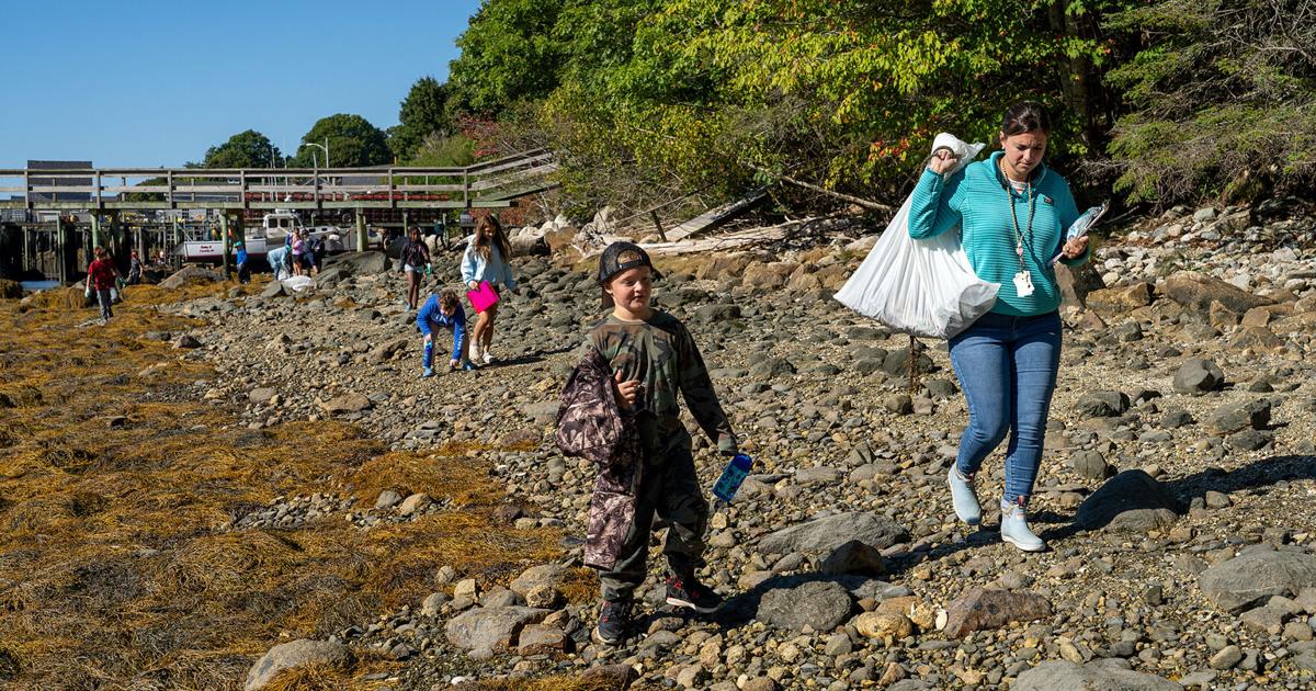 Elementary students in gloves collect trash along rocky Maine shoreline near town wharf