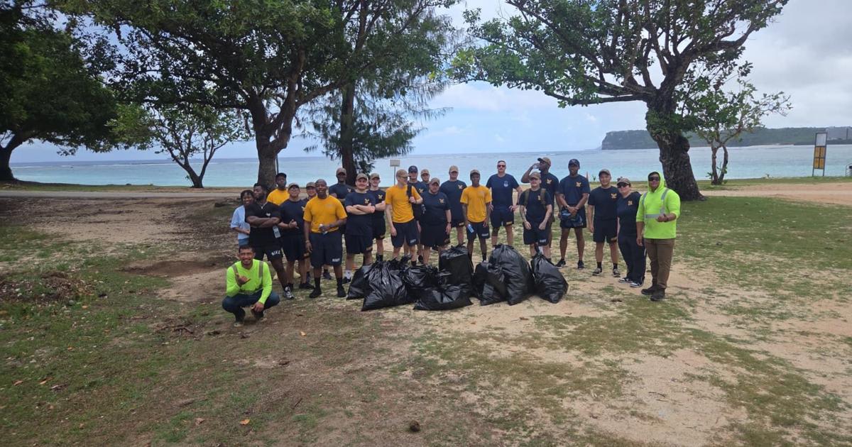 Navy sailors in work clothes picking up trash and debris at tropical beach park in Guam