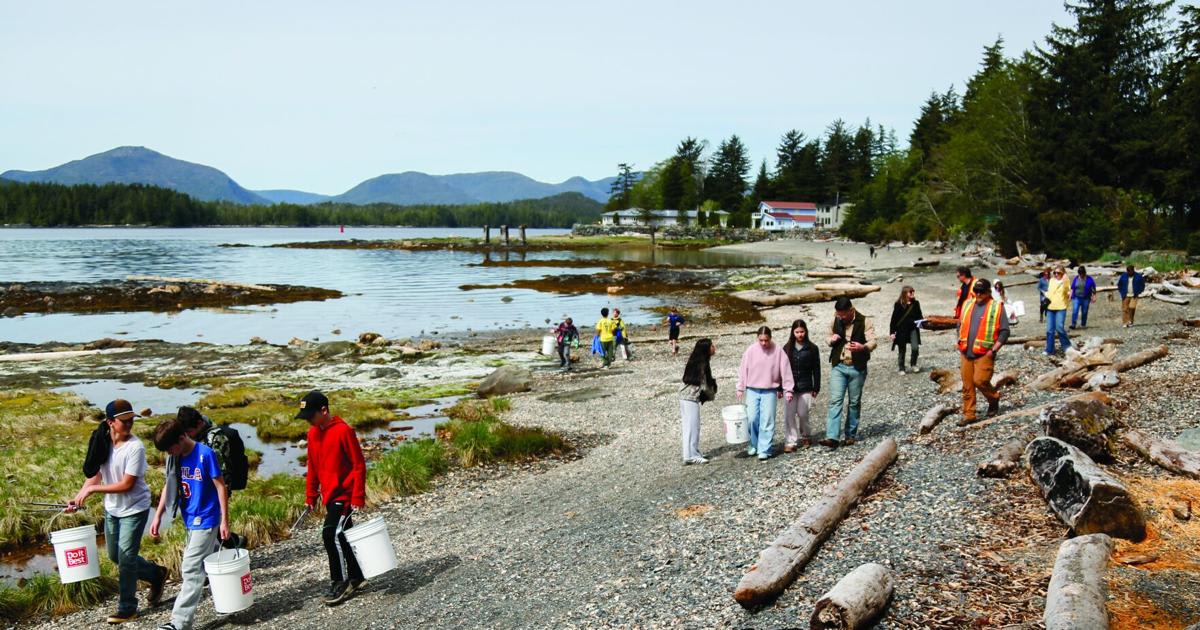 Students walking along Alaska beach carrying blue buckets to collect litter from cleanup station