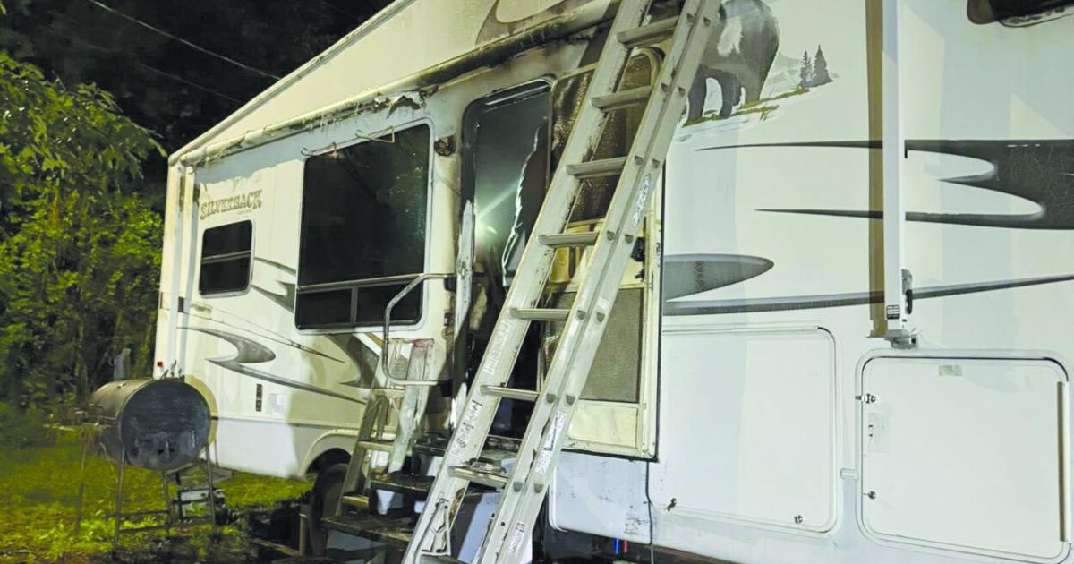 Firefighters responding to fully engulfed camper fire with flames visible above treeline at night