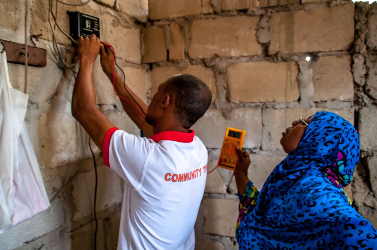 Women installing solar panels on rooftops in rural Zanzibar village bringing clean electricity