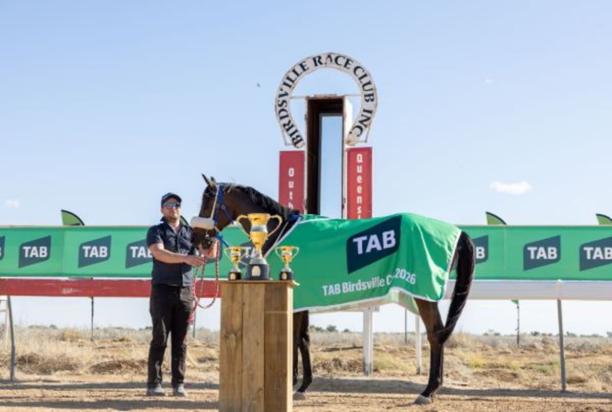 Racehorse Raetihi crossing finish line at Birdsville Cup in Queensland's red desert landscape