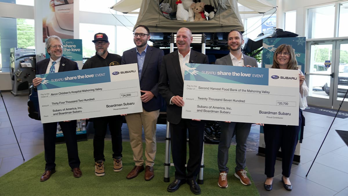 Boardman Subaru dealership staff and charity representatives holding large donation checks outside showroom