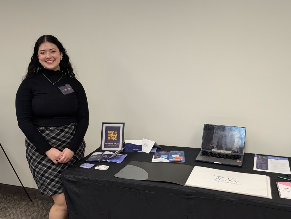 Marzena Krulik standing beside her exhibition booth displaying graphic design portfolio work and promotional materials