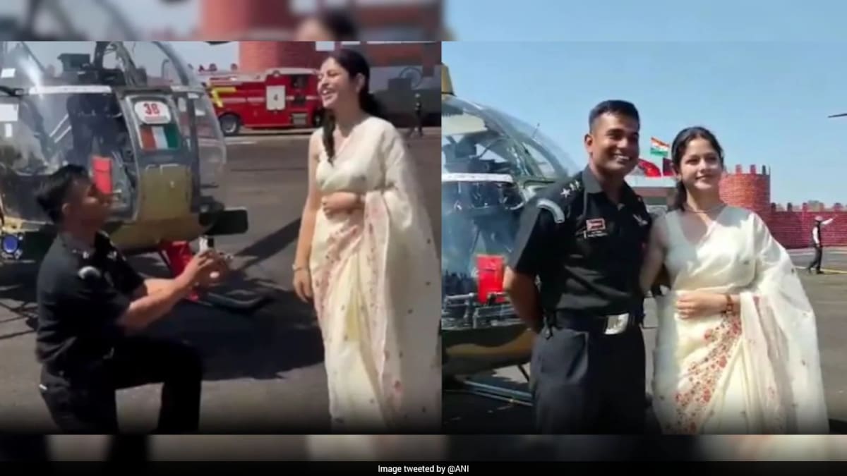 Indian Army pilot in ceremonial uniform kneeling before girlfriend with helicopter in background
