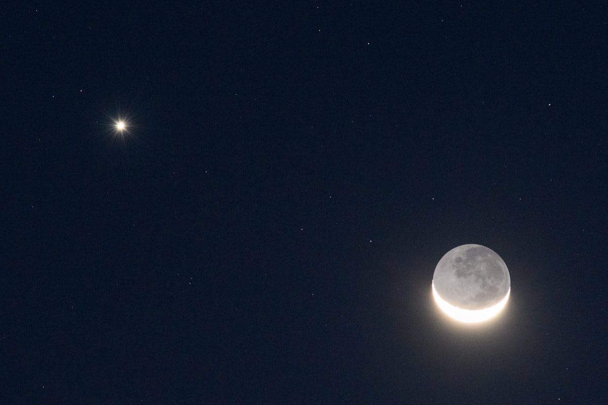 Thin crescent Moon appearing between bright Venus and Jupiter in twilight western sky