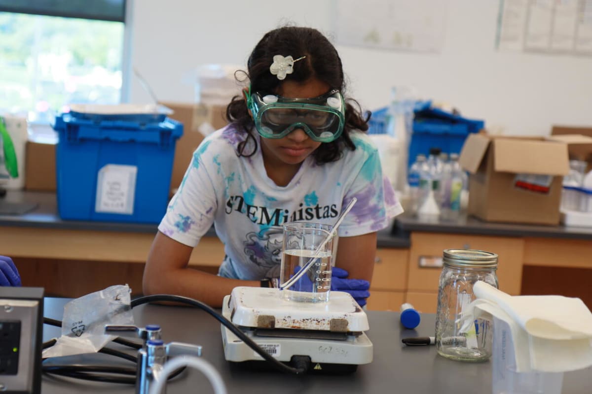 Middle school girls in lab coats conducting biotechnology research with college mentors at Albany summer camp
