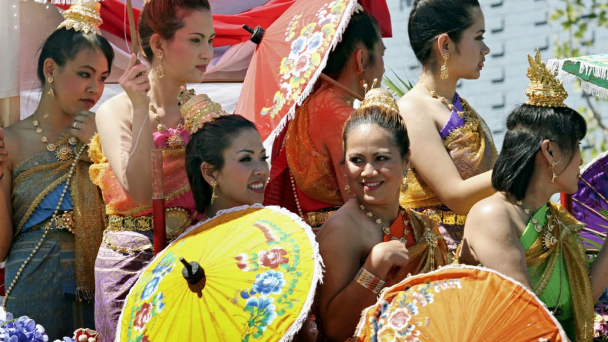 Chefs preparing traditional Pad Thai noodles in large woks at outdoor festival celebration