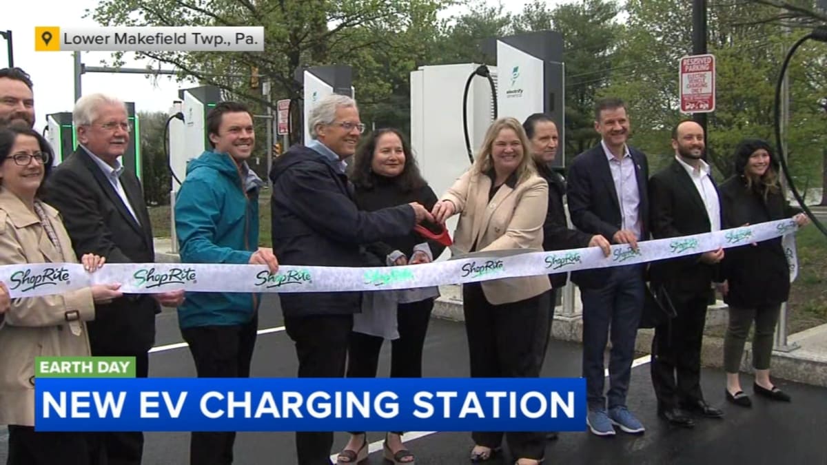 Six white electric vehicle charging stations outside ShopRite grocery store with ribbon cutting celebration