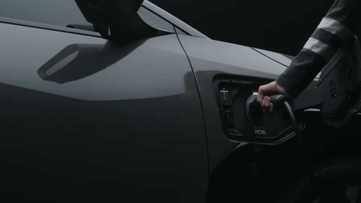 Person plugging electric vehicle charger into car in residential driveway, sunny day