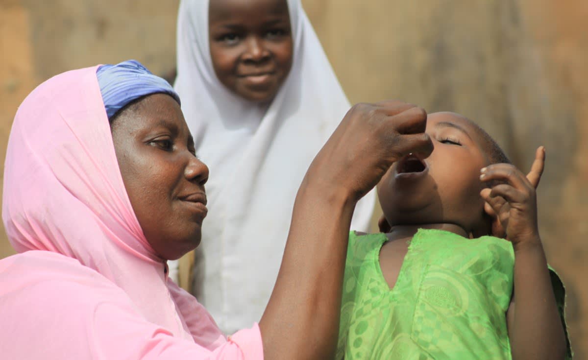 African female health worker in uniform administering vaccine to smiling child in rural community setting