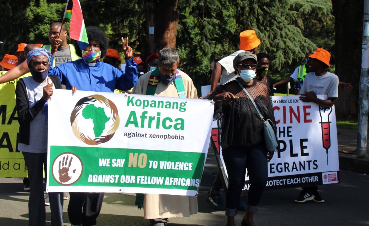 South African flag flying with people walking peacefully in an urban community setting