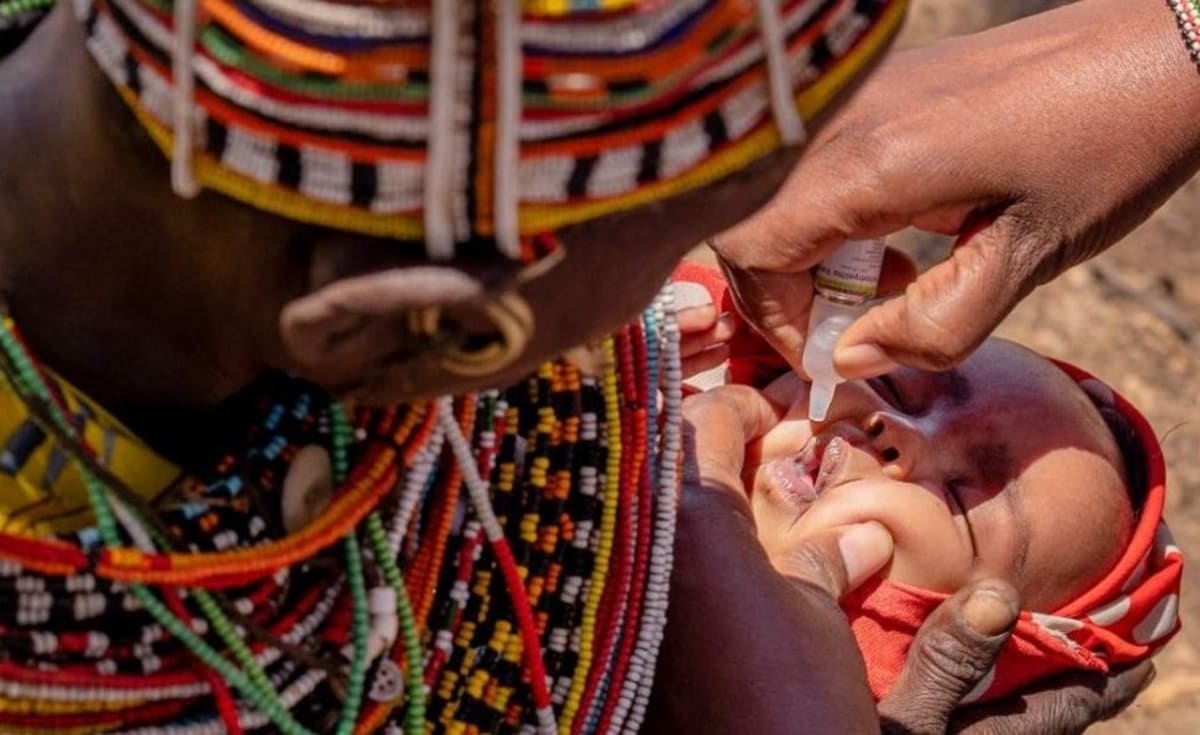 African healthcare worker administering vaccine to smiling child while mother watches nearby