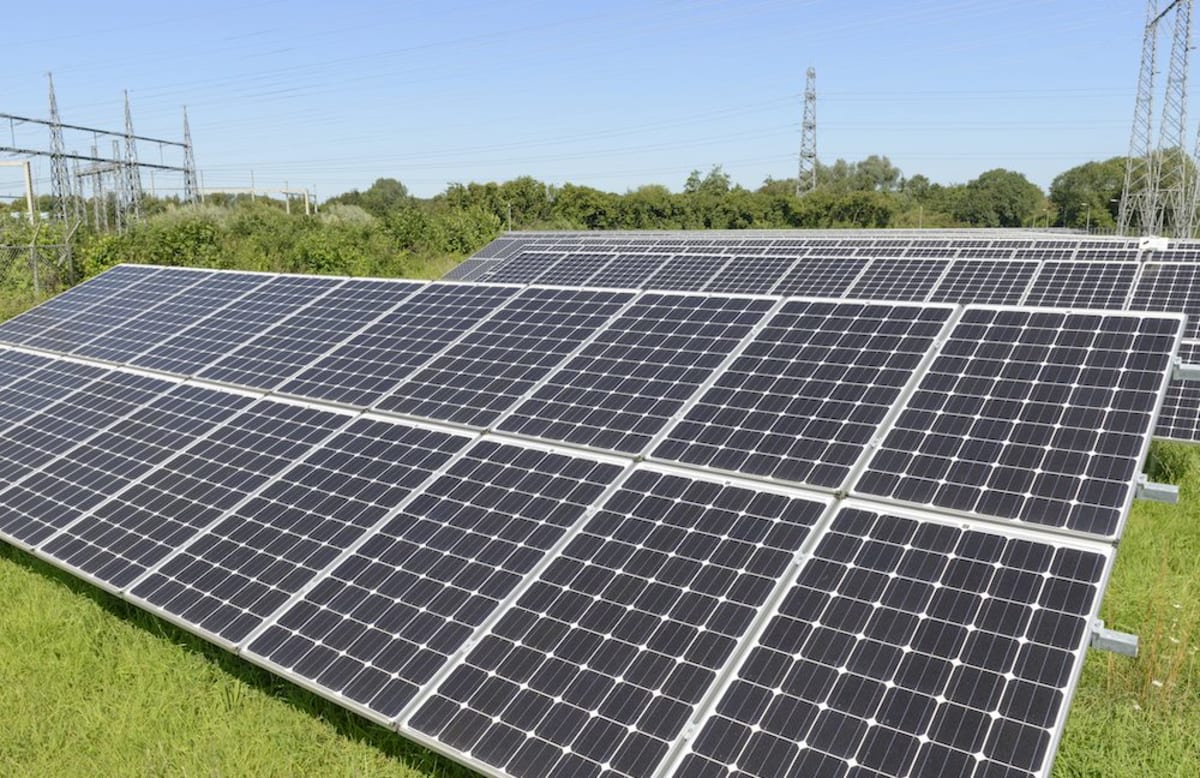 Solar panels reflecting sunlight with electricity transmission towers in background against blue sky