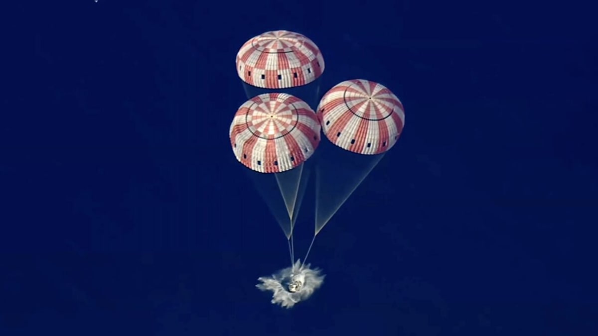 NASA Orion spacecraft descending on three orange and white parachutes over Pacific Ocean