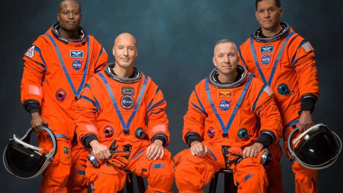 ** Four astronauts in blue flight suits smile at NASA event announcing Artemis III crew