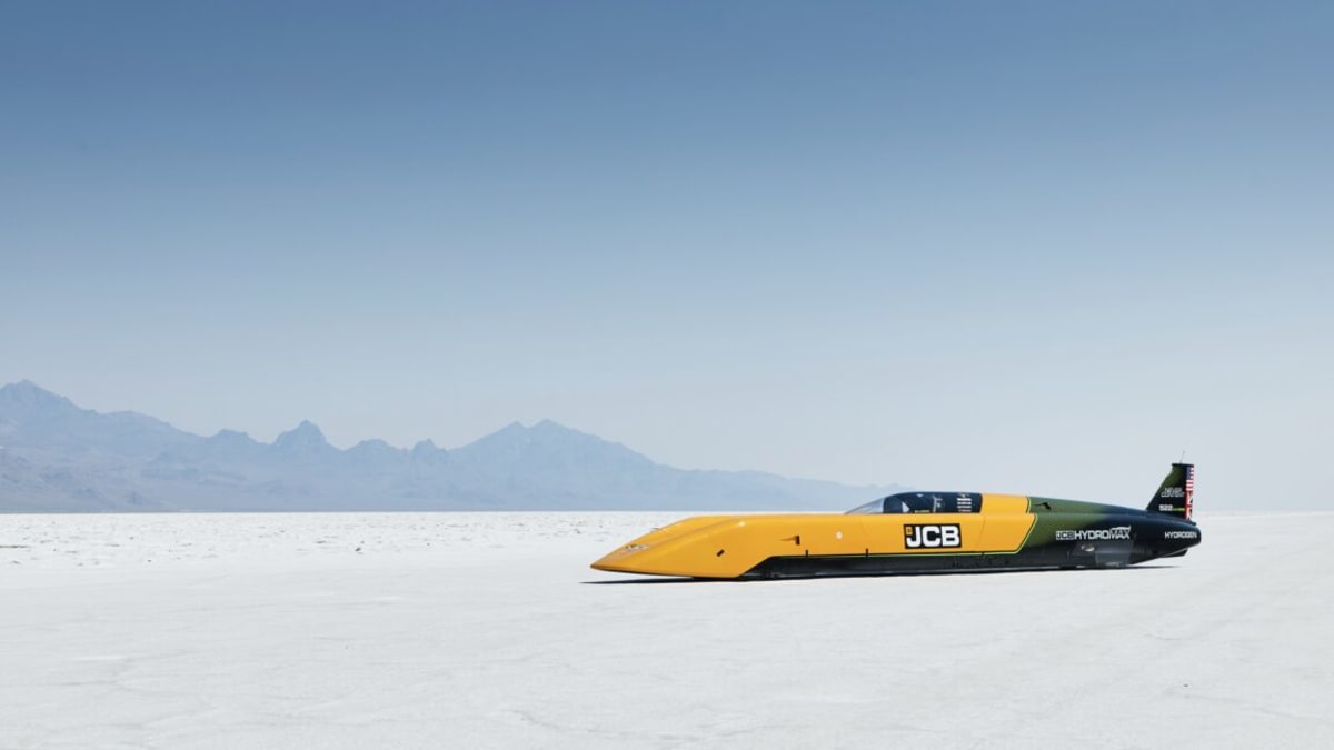 Streamlined silver JCB Hydromax racing car on white salt flats with crew celebrating record