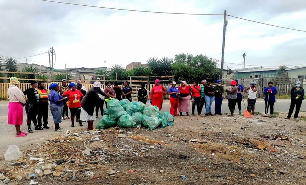 Volunteers wearing gloves collect trash bags during community cleanup in Nelson Mandela Bay