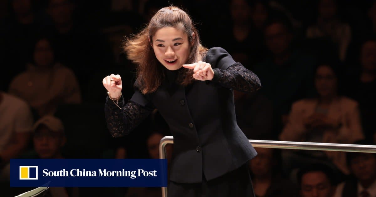 Conductor Elim Chan standing in front of San Francisco skyline holding baton